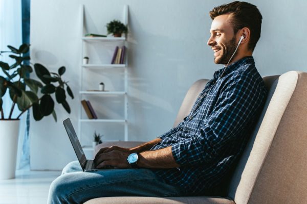 side view of smiling man in earphones taking part in webinar at home side view of smiling man in earphones taking part in webinar at home